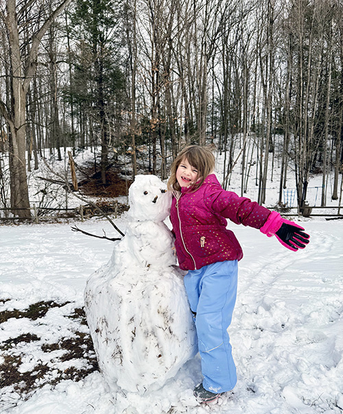 School girl smiling next to a snowman