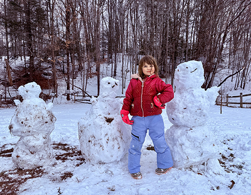 School girl posing for a picture with three snowmwn